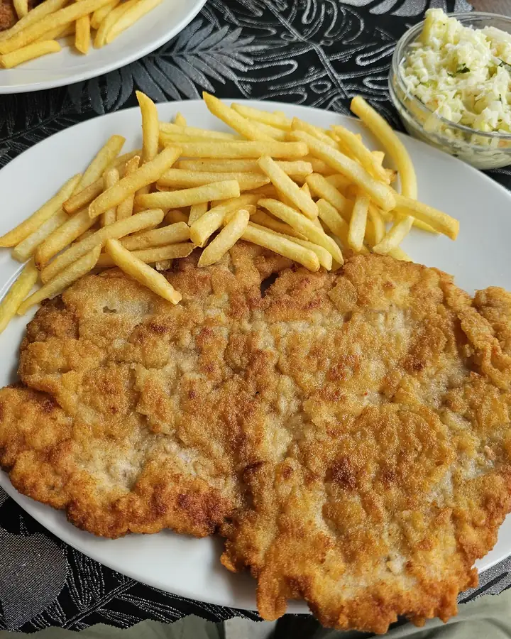 Duży kotlet schabowy z frytkami i surówkami na stoliku w Barze Karolinka