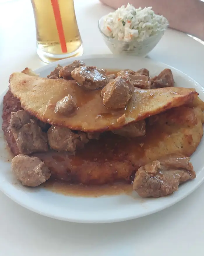 Placek ziemniaczany przykryty gulaszem, obok surówka